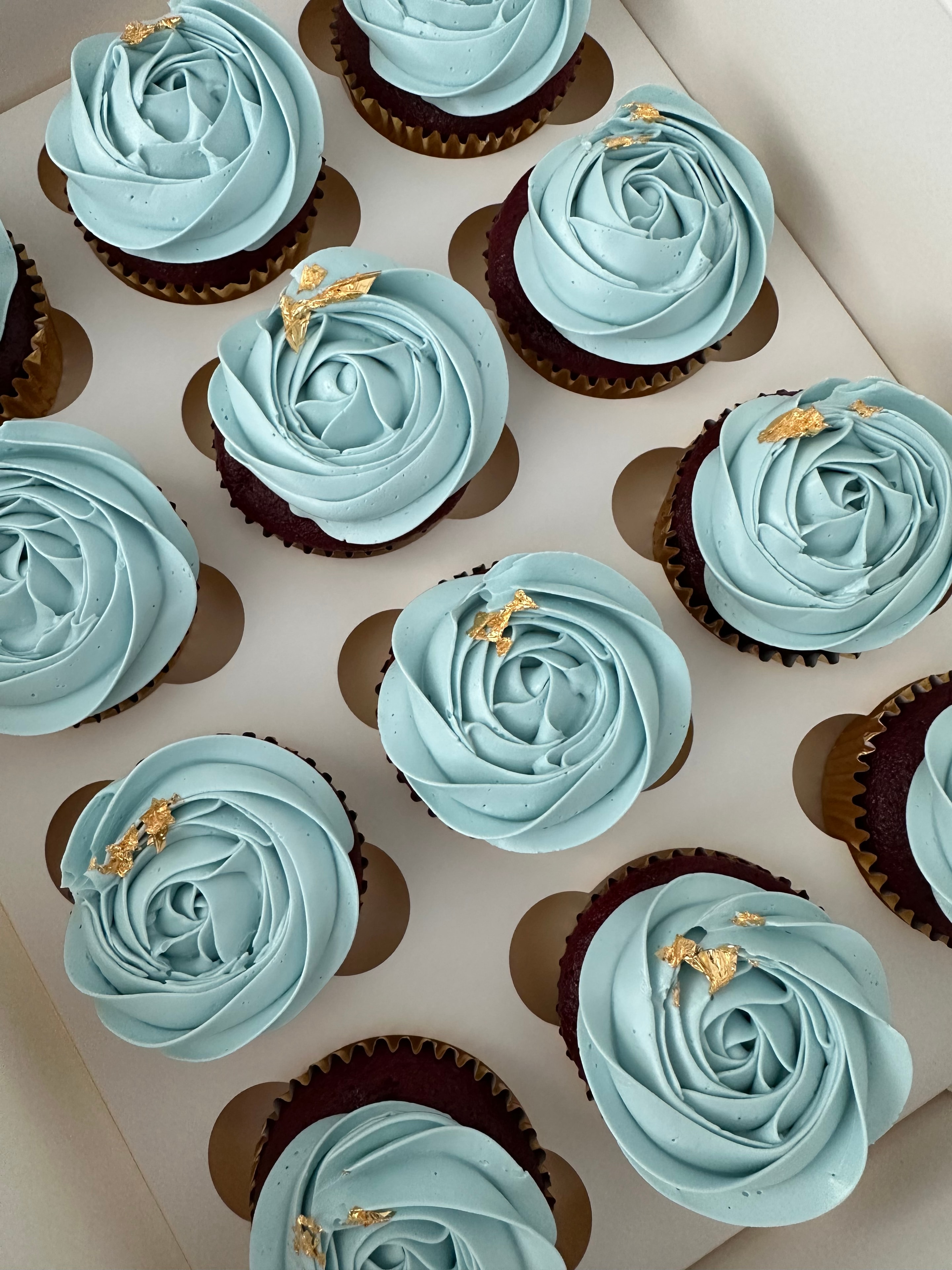 Elegant rose-piped cupcakes with light blue frosting and gold leaf