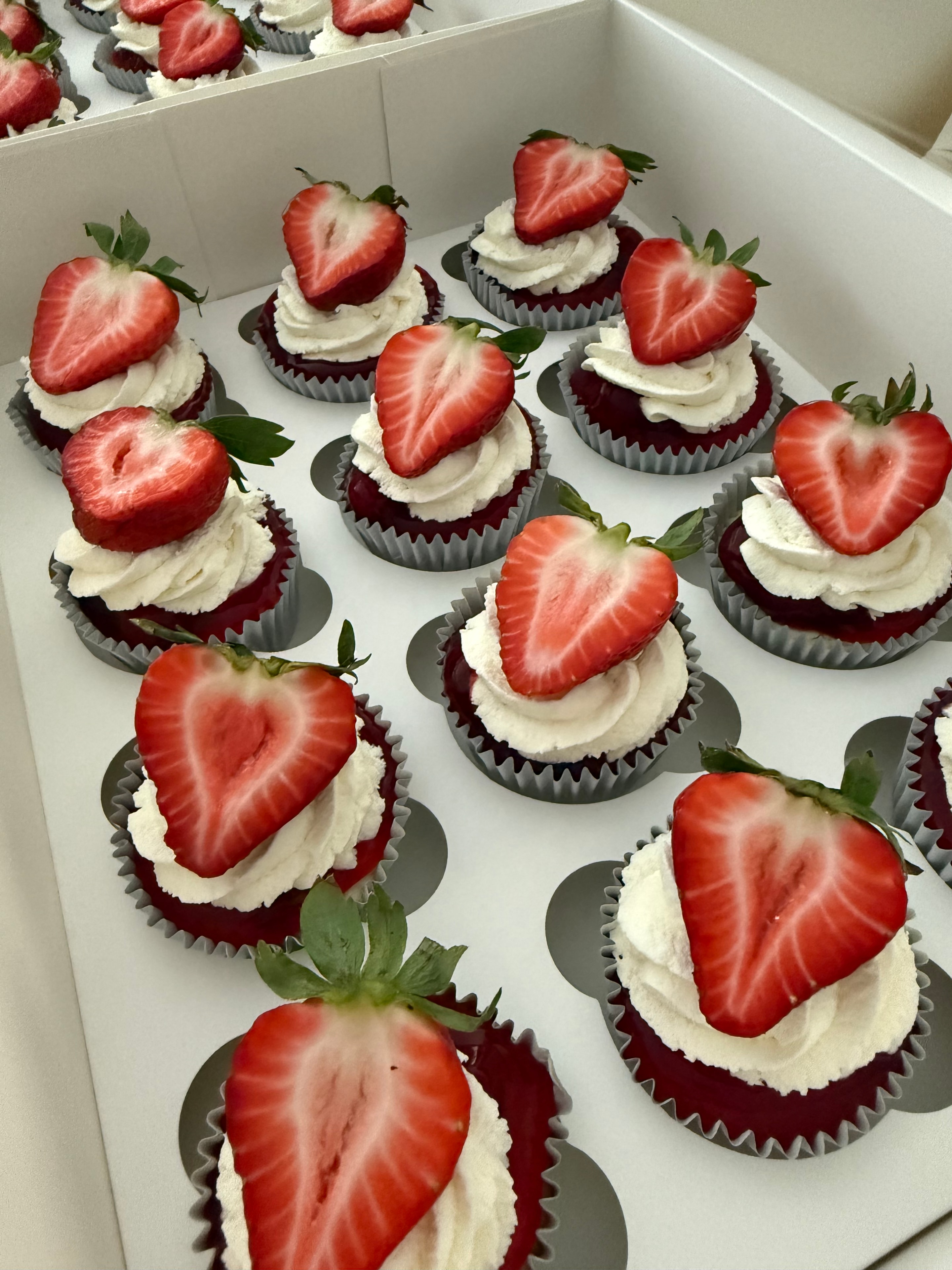 Red velvet cupcakes topped with fresh strawberries and cream cheese frosting